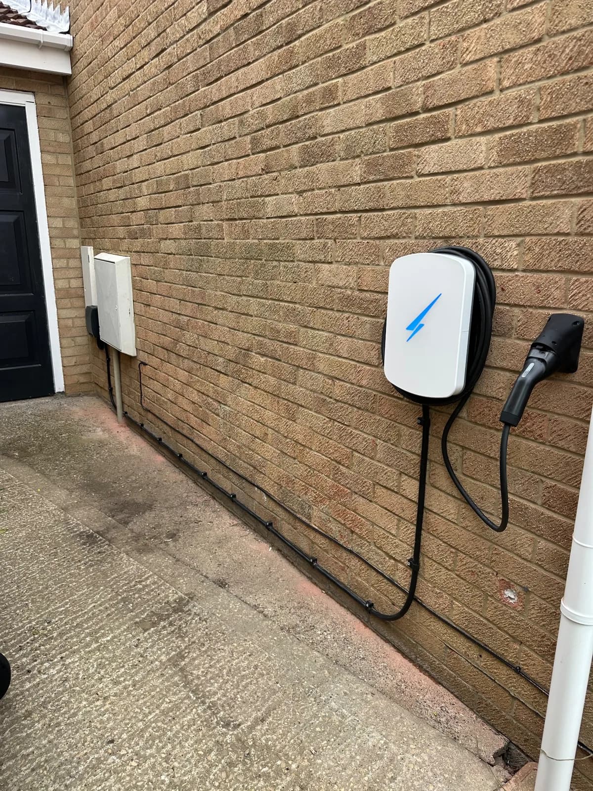 White EV charger on a side wall, with the supply cable clipped neatly along the base of the brickwork from the meter box